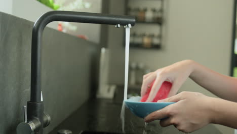 las manos de los niños lavando un plato sucio bajo el agua corriente de un grifo de la cocina