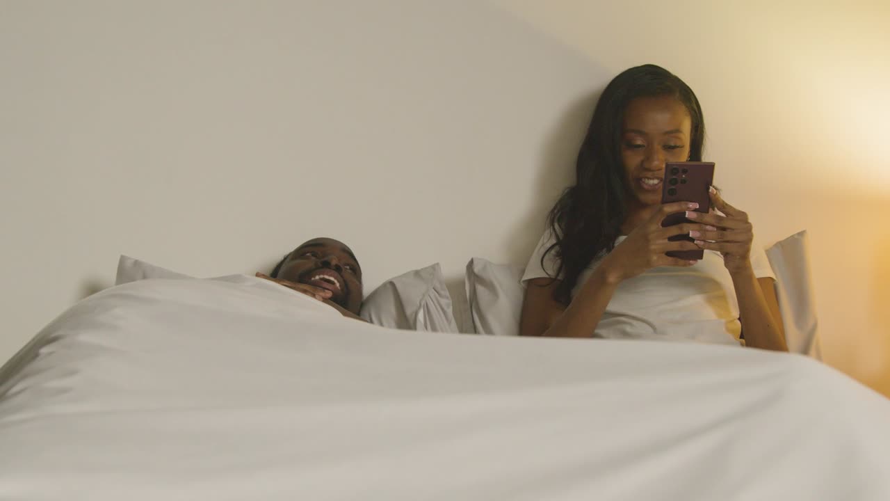 Couple At Home At Night Lying In Bed With Woman Looking At Mobile Phone 3