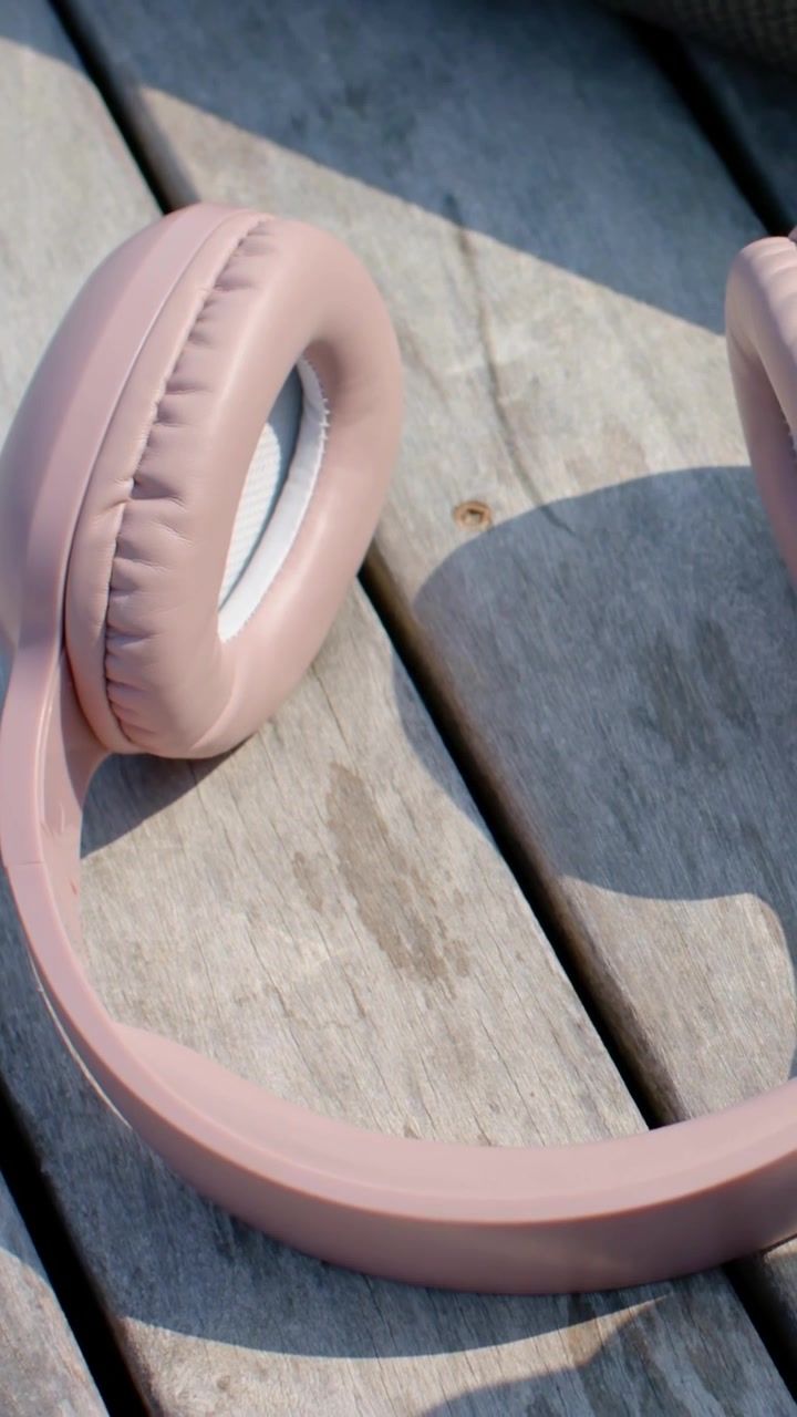 Video verticale: Telecamera portatile che registra, panoramica su una panchina esterna per mostrare auricolari rosa pastello.
