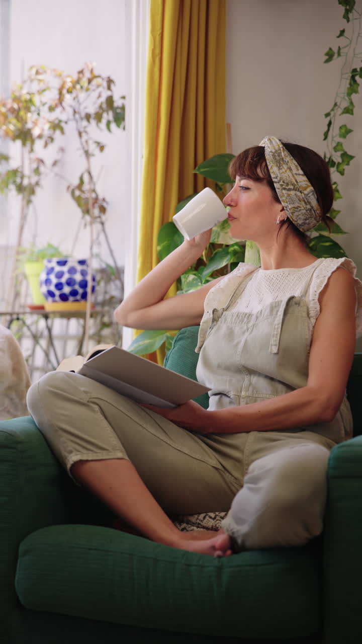 Kvinde læser en bog og drikker kaffe, mens hun sidder med sin hund derhjemme. Hyggeligt livsstilsøjeblik, afslapning og selskab i et varmt indendørsmiljø.