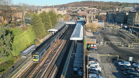 Cinematic-aerial-drone-footage-of-train-leaving-the-train-station-with-platform-and-carpark-Dewsbury-UK