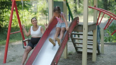 pregnant mother watching daughter play on slide at playground