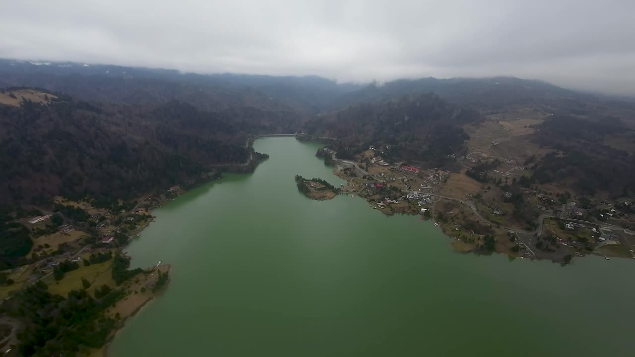 vista aérea de un lago sinuoso rodeado de colinas y comunidades rurales bajo un cielo nublado con una pequeña isla en el lago