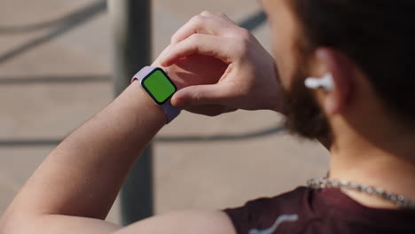 athletic man looking at left hand with smartwatch chroma key touching interacts with green screen