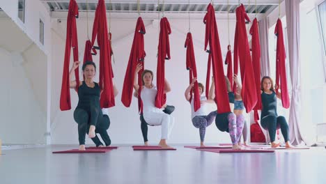 concentrated women perform stretching poses using hammocks