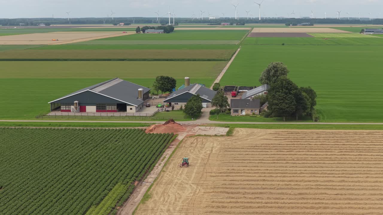 Landbrugstraktor arbejder på bearbejdet mark, bondegård og siloer i syne, Holland