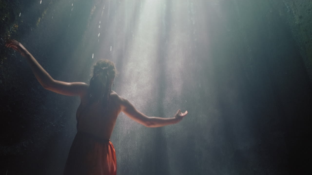 mujer feliz bailando en la cueva de la cascada salpicando agua usando un hermoso vestido disfrutando de la naturaleza bailando sintiendo libertad espiritual 4k