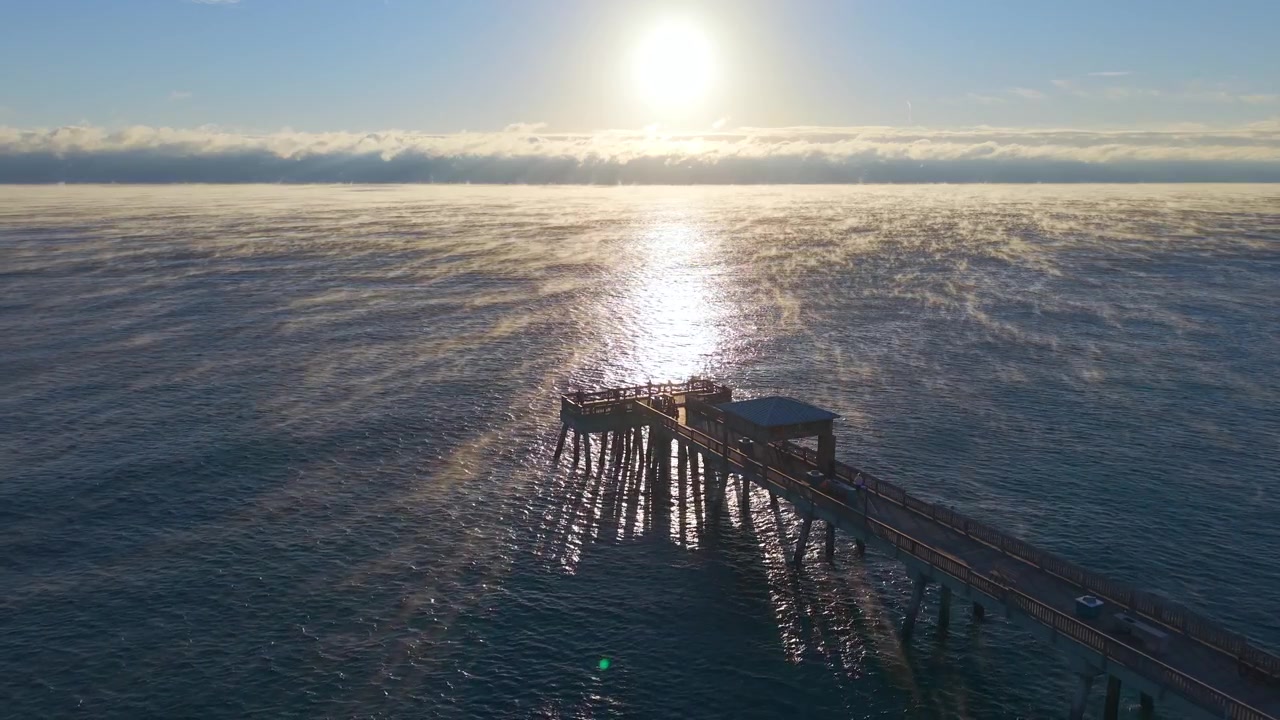 Stationary aerial drone shot of the Deerfield Beach pier on a cold morning at sunrise with steam rising off the ocean surface