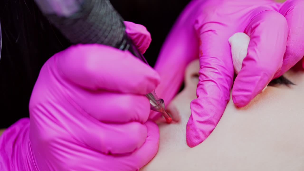 Lips tattoo procedure. Cosmetologist in pink gloves doing lips permanent makeup for female client in a beauty spa. Close-up.