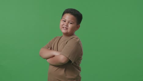 side view of asian boy crossed arms and warmly smiling on green screen background in the studio