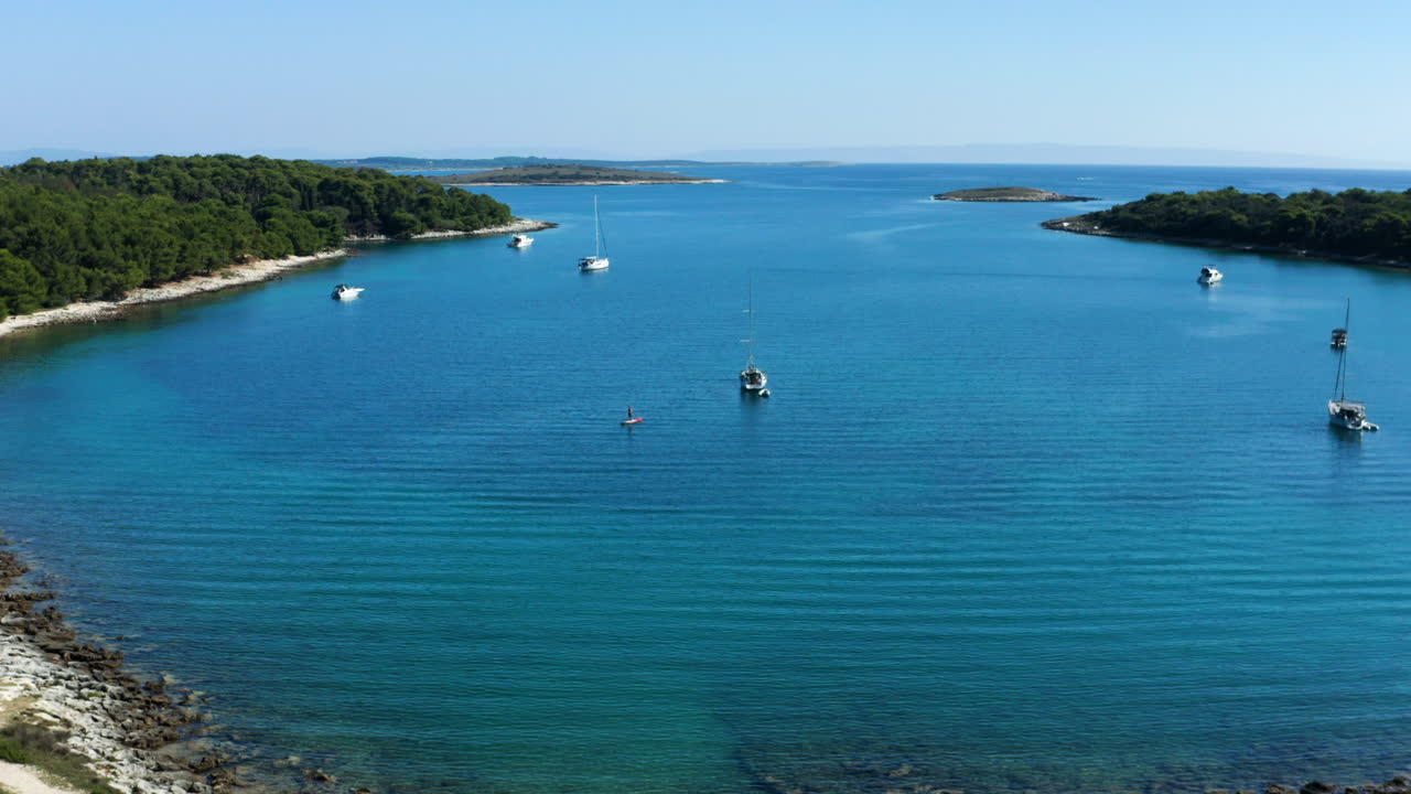 vista aérea de barcos flotando en uvala soline con coche azul conduciendo en una pista todoterreno en cabo kamenjak, pula, croacia