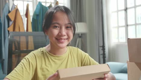 Close Up Of Asian Young Girl Online Seller With Package Look At Camera And Smile While Selling Clothes At Home