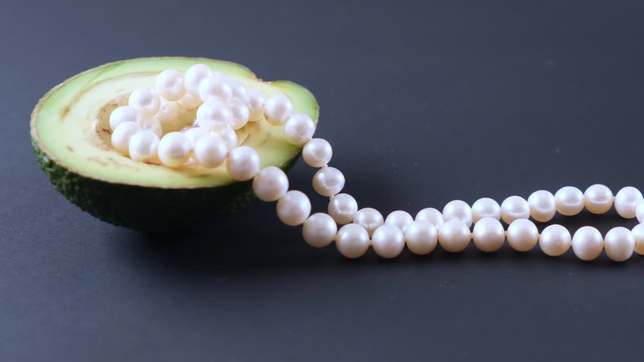 la mitad de un aguacate con perlas en un fondo negro. surrealismo. diseño de alimentos de moda