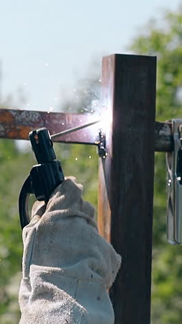handyman in mask and work gloves welds metal parts of country house fence slow motion backside view