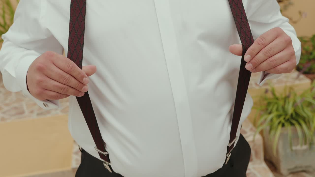 Close up of man adjusting suspenders on white dress shirt before event