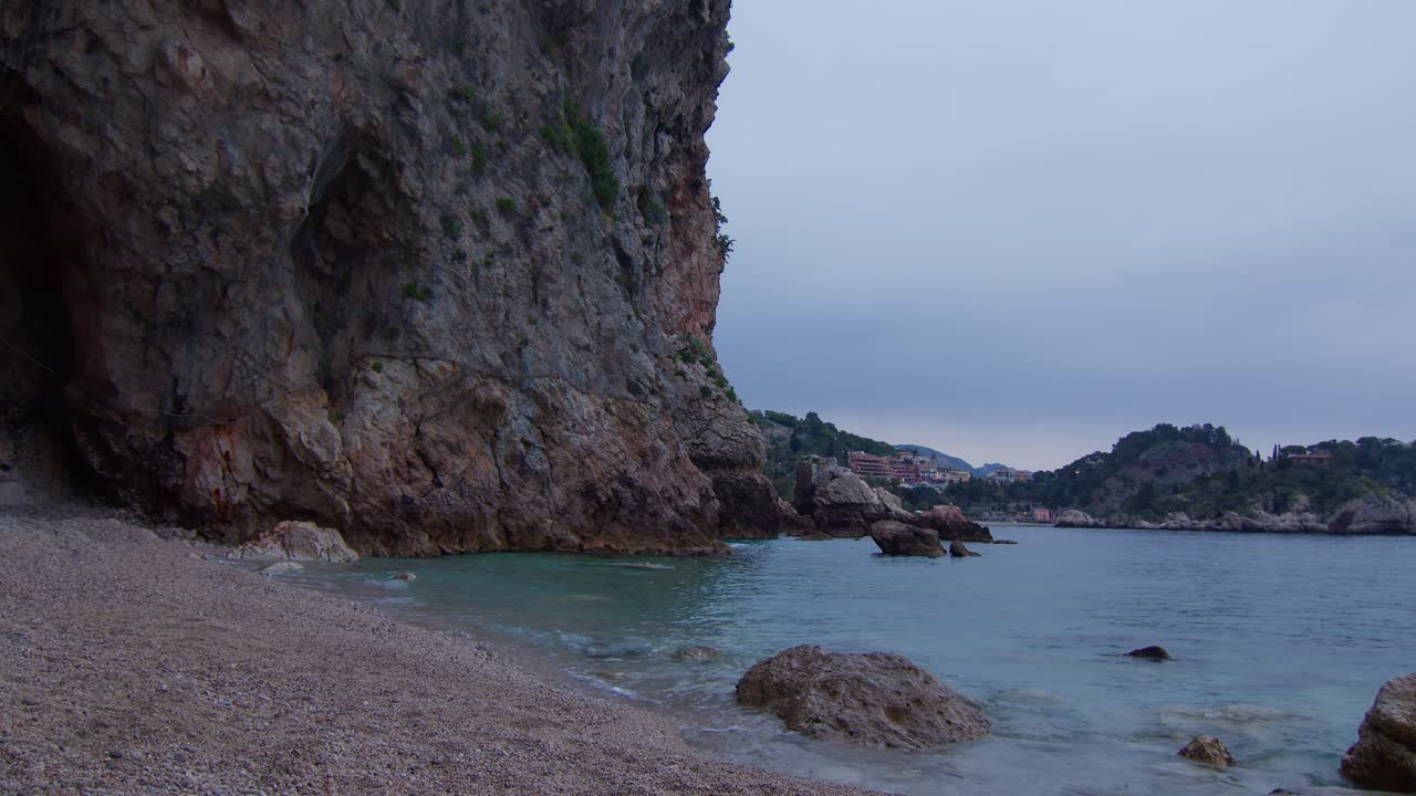 Static shot of calm waves on hidden cave beach with Isola Bella in background in Taormina, Sicily, Italy (Sicilia, Italia), cinematic and serene