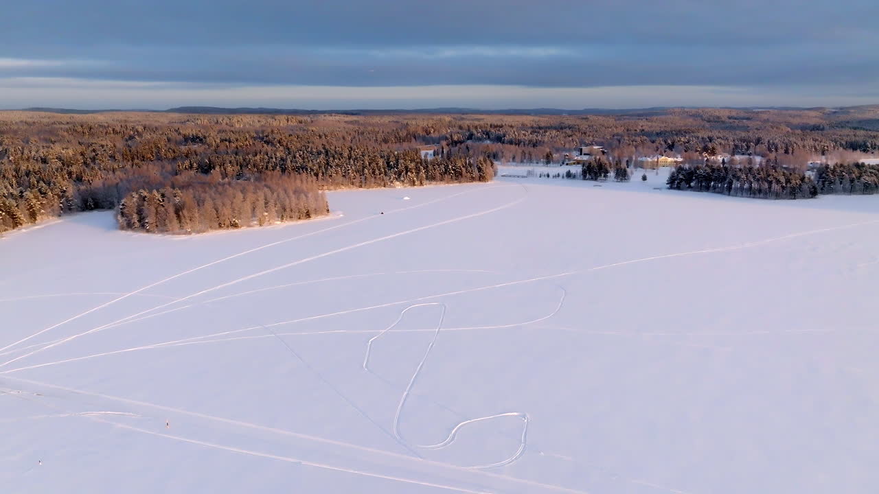 Wide drone shot following a snowmobile driving on a lake ice, sunrise in Finland
