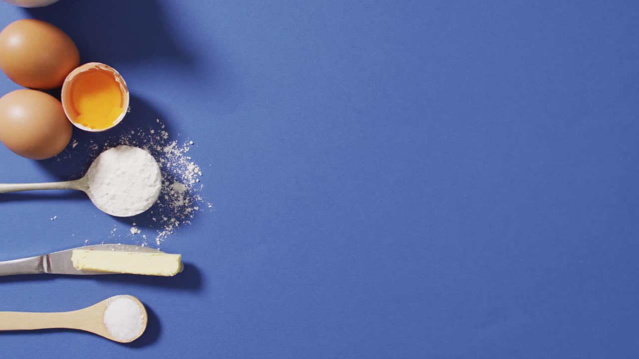Video of baking ingredients and spoons lying on blue surface with copy space