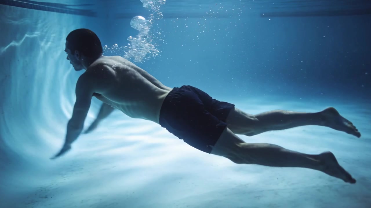 Nuotatore maschio in piscina che parte, scalcia, espira bolle, si inclina per respirare, con costume scuro e increspature.