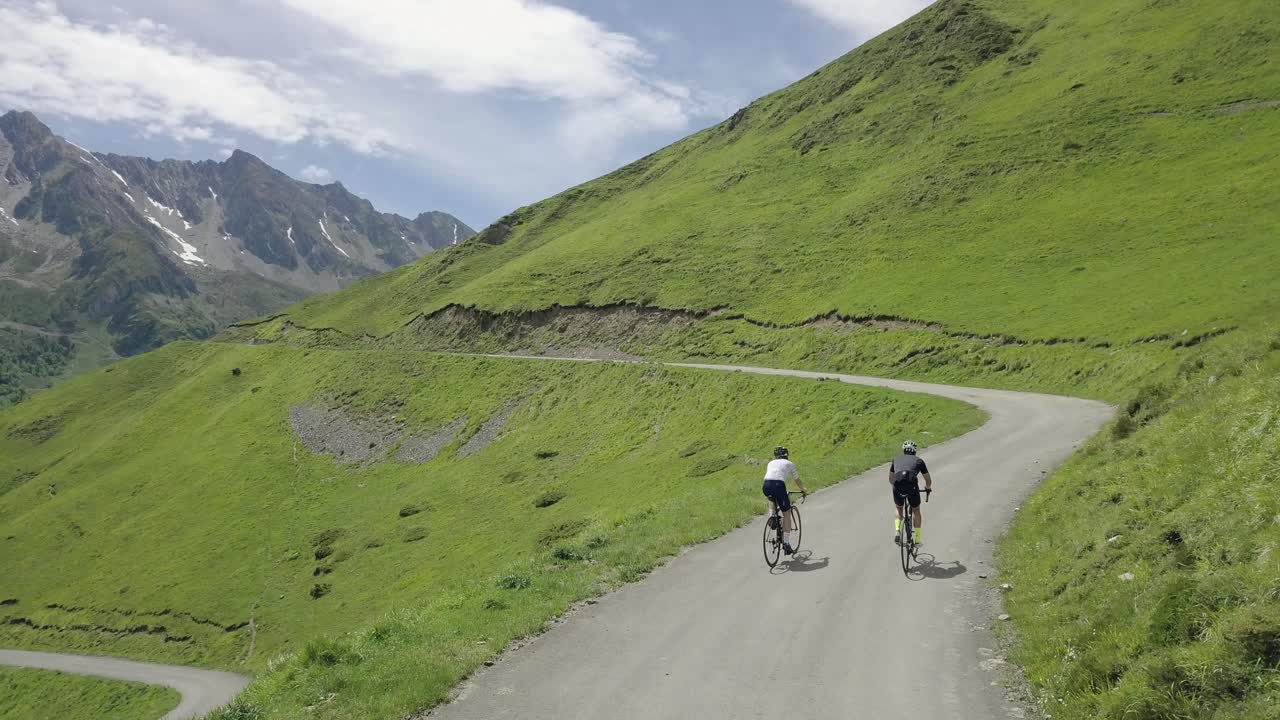 Drone aerial behind view following two unrecognisable cyclists on an incredible mountain with an epic scenery