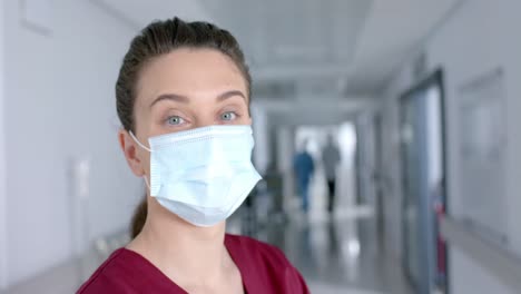 portrait of happy caucasian female doctor wearing face mask in corridor, slow motion