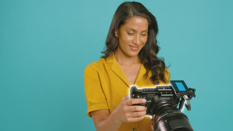 Motion-Graphics-Around-Female-Videographer-With-Camera-Filming-Video-On-Blue-Background-In-Studio