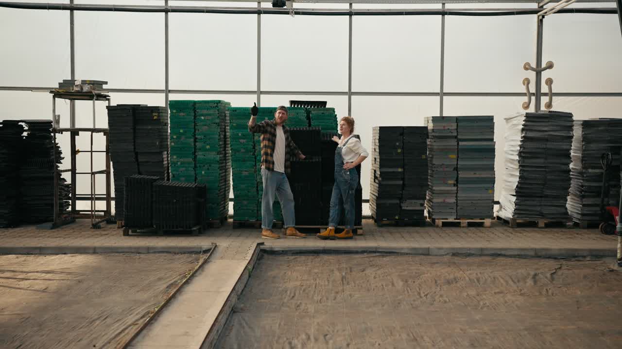 un granjero confiado en una gorra junto con su novia de cabello rojo diseñando la disposición de las plántulas en un invernadero en una granja