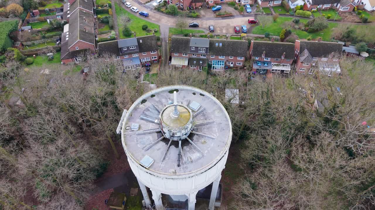 Drone-tilbagetrækning fra Bengeo vandtårn, oppefra, kamera låst på tag og telekommunikationsmast, derefter udvides billedet for at afsløre omkringliggende huse, veje og træer i Hertford, England