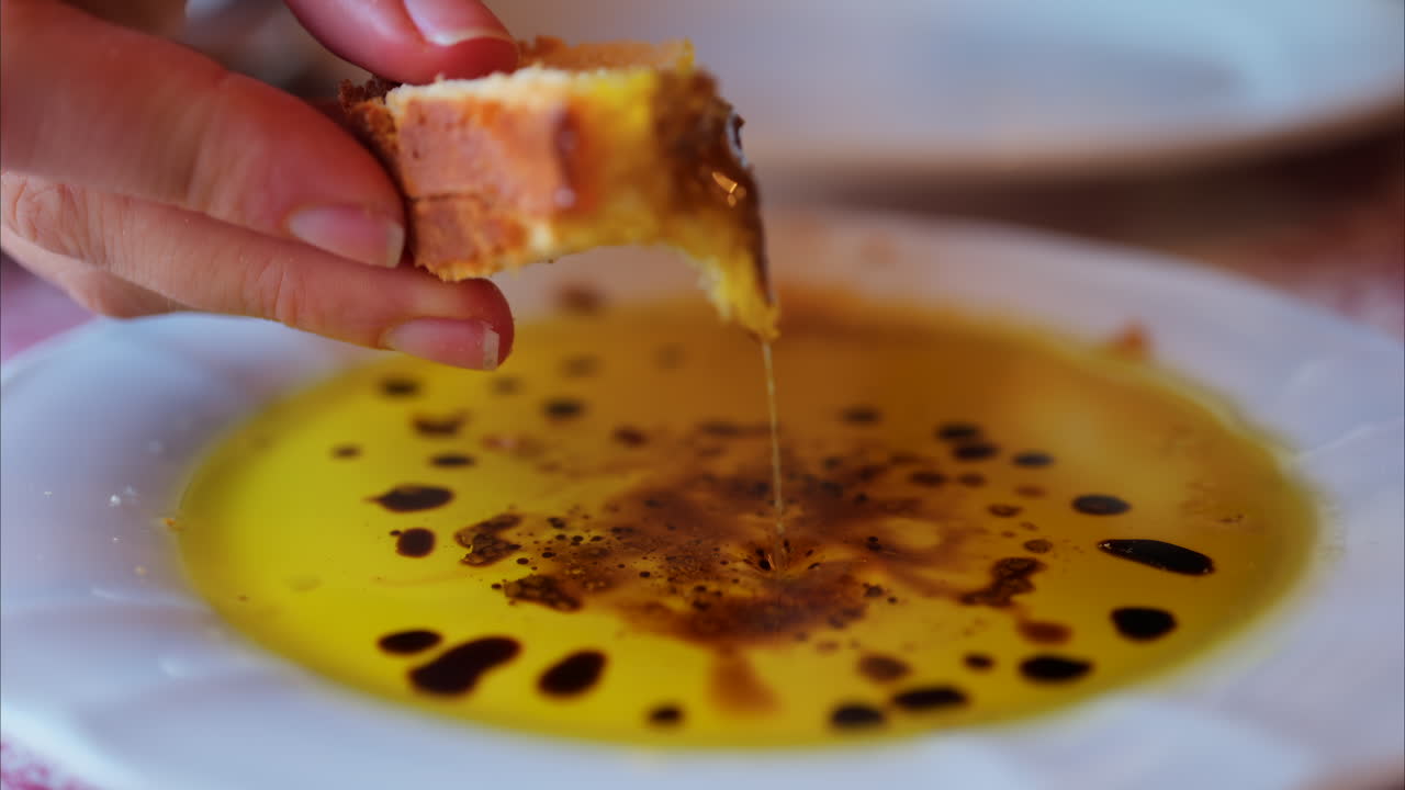 Close up of a woman dipping bread in olive oil with balsamic glaze drops and eating it at a restaurant