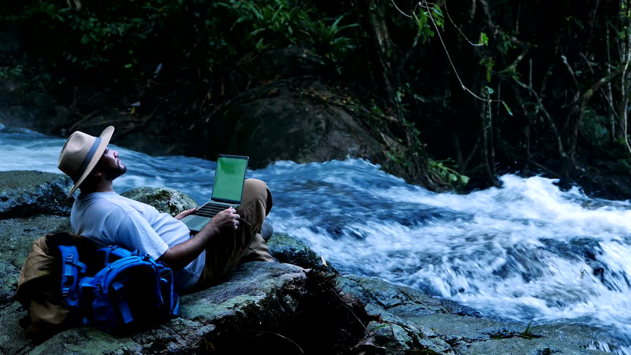 녹색 화면 노트북 컴퓨터를 사용하는 젊은이가 폭포에서 여행과 프리랜서 작업 개념