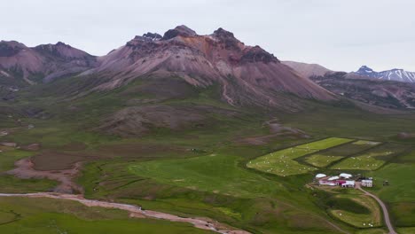 Colorful-volcanic-mountain-with-sheep-farm-in-valley,-aerial