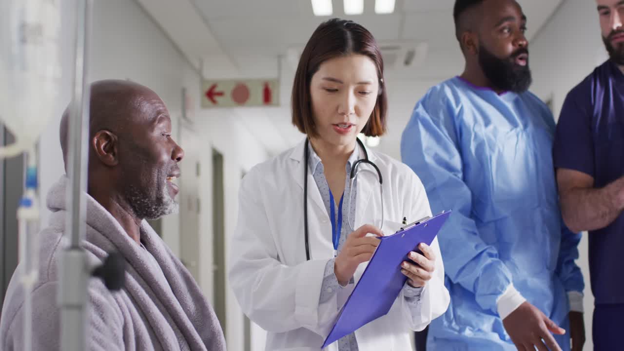 Video of diverse male patient and female doctor writing notes talking in busy hospital corridor