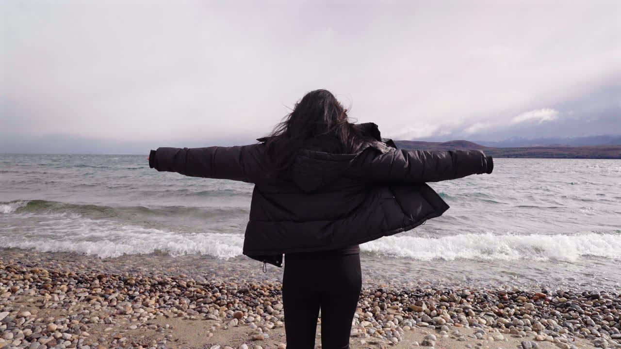 Forward moving clip captures fearless female standing against the wind, with waves thrashing as sunlight breaks through clouds. Ideal for liberation or self-discovery narratives