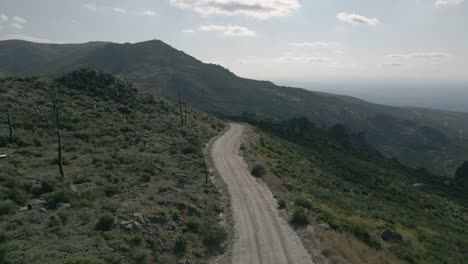 Winding-dirt-road-leading-over-the-mountains-with-short-bushes-and-dead-trees