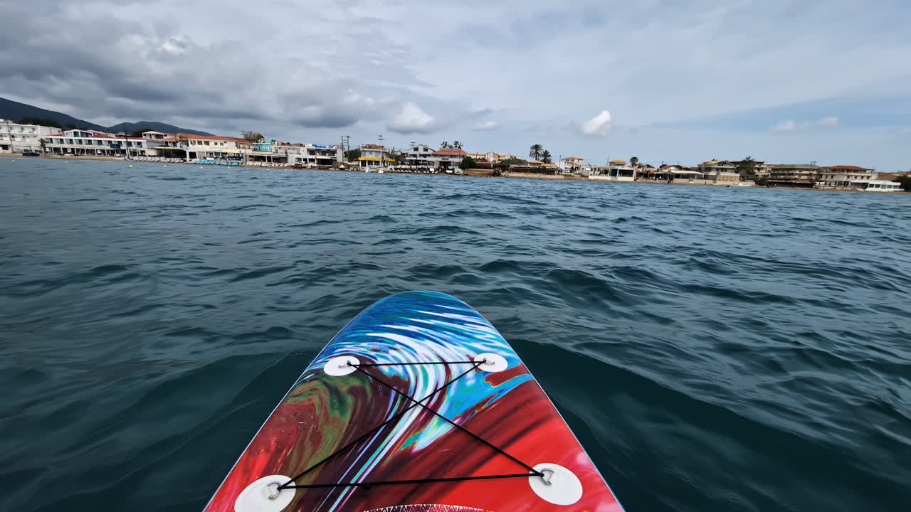 POV shot of a kayaker on kayak to a city on coast of sea under a cloudy day.
