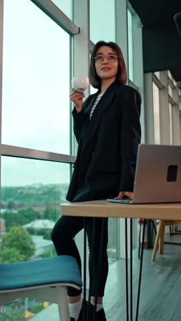 business lady drinking coffee looks at her laptop. receiving a message via mail during lunchbreak. low angle view. vertical video.