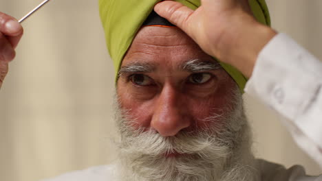 fotografía de estudio de cerca de un anciano sikh con barba usando la aguja salai al ponerse el turbante contra un fondo plano 3