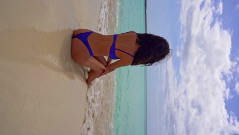 Vertical-shot-of-pretty-brunette-girl-sitting-on-shore-of-Caribbean-Sea-and-enjoying-beautiful-weather-during-holidays