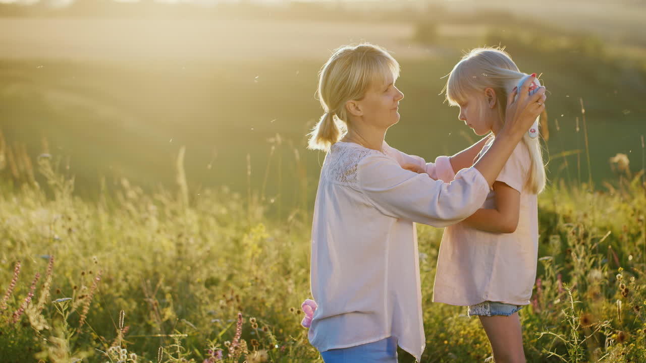 야외에서 그녀의 딸을 빗질하는 금발 머리를 가진 젊은 어머니