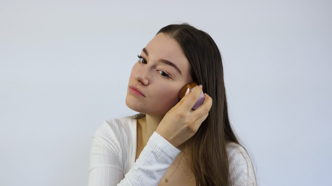 concentrada hermosa mujer joven haciendo su maquillaje delante del espejo con el pincel