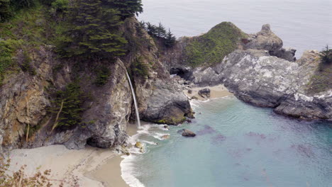 mcway falls cascading on the beach in a secluded cove - zoom out reveal