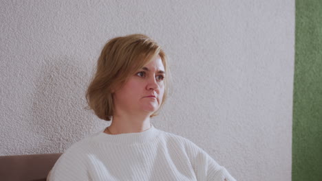 reflective soul seated on sofa looking thoughtful against green accent wall wearing white sweater and neutral pants absorbing session atmosphere in modern therapy space during evening light