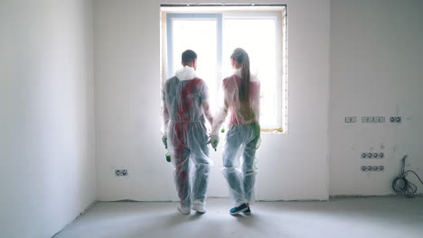 couple in protective suits comes to window joining hands