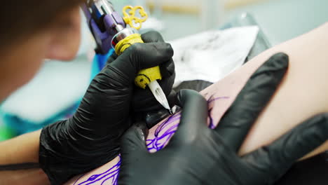 artist of tattoos at work. tattooist wearing black latex gloves applies the ink on the picture on customer's hand.