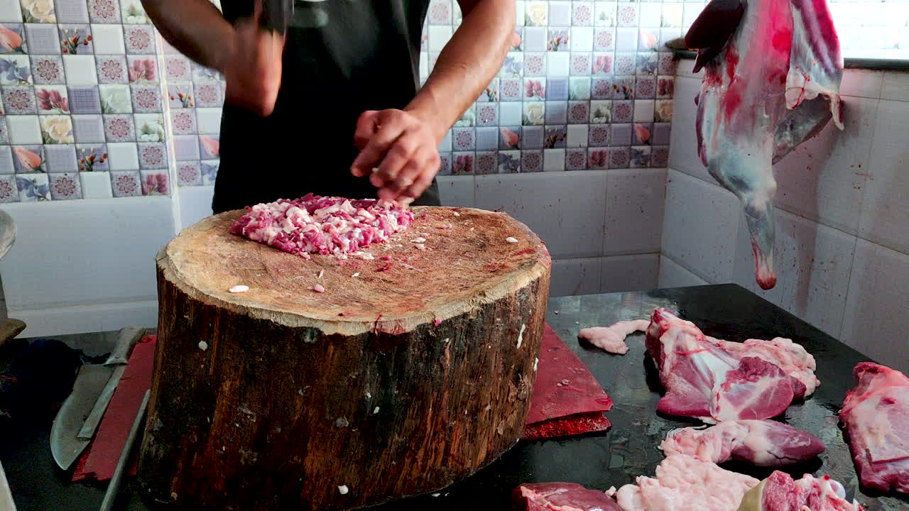 Asian Male Butcher Minces Red Meat on a Wooden Trunk At Shop.