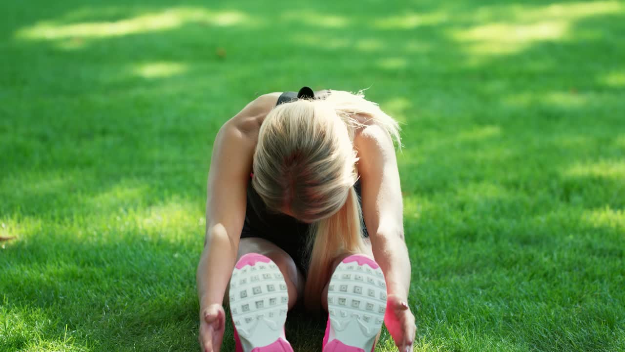 Fit woman doing stretching gym on green grass in summer park.