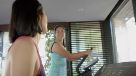 Happy-asian-female-friends-exercising-and-smiling-in-sunny-home-gym,-slow-motion