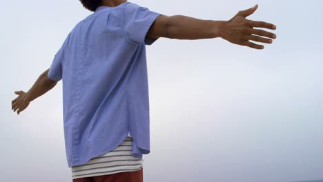 Low-angle-view-of-African-American-man-standing-with-arms-outstretched-on-the-beach-4k