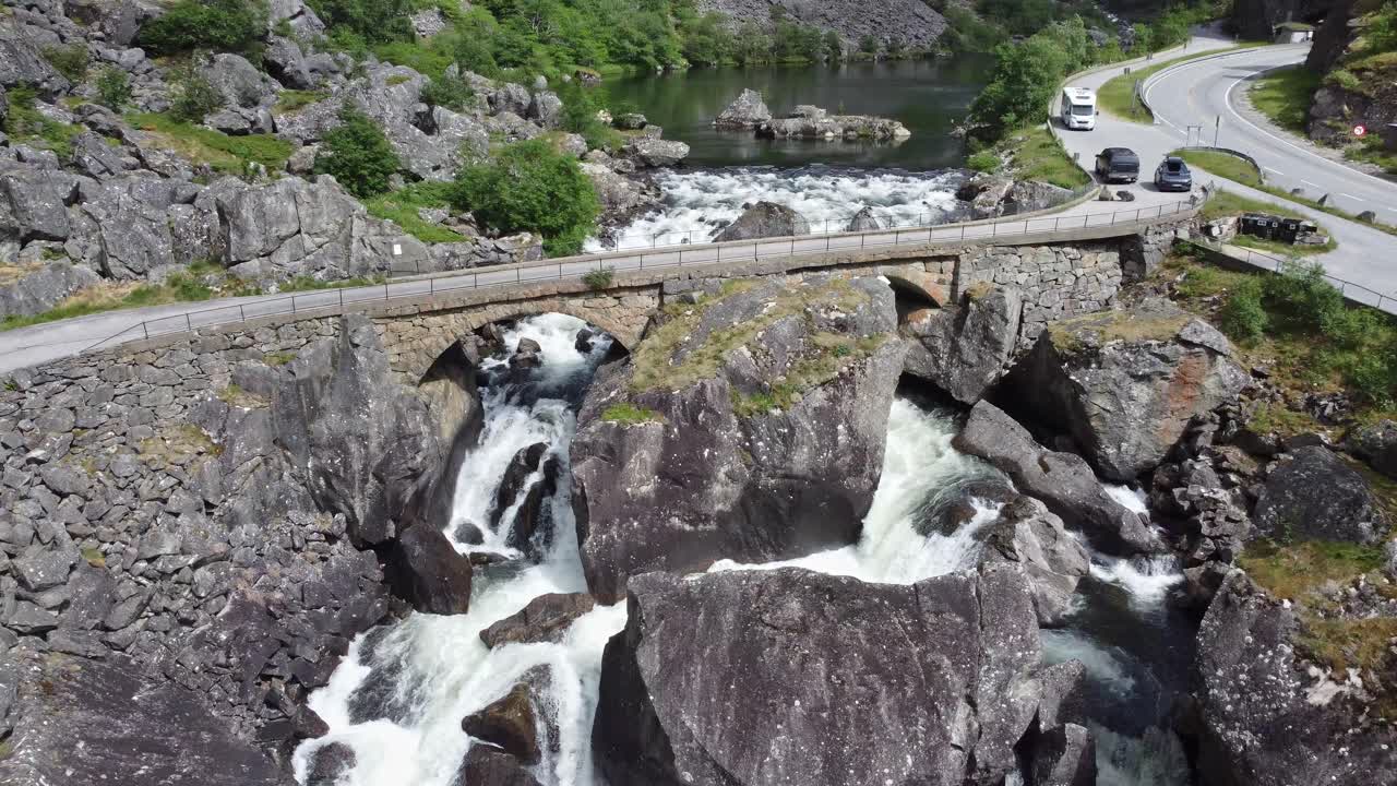 carretera que cruza el viejo puente construido por rocas - río que fluye desde el lago y debajo del puente - valle de mabodalen noruega aérea