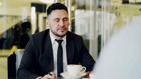 bearded caucasian businessman gesticulating and discussing his startup plan with investor in formal wear in glassy cafe during during meeting